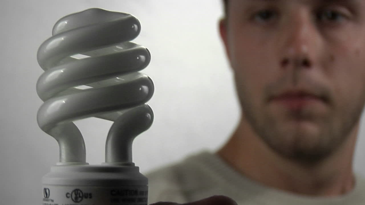 un joven mira una bombilla fluorescente compacta mientras se enciende