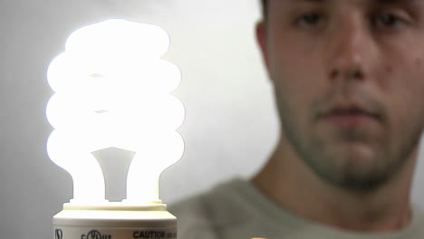 a young man gazes at a compact fluorescent light bulb as it lights