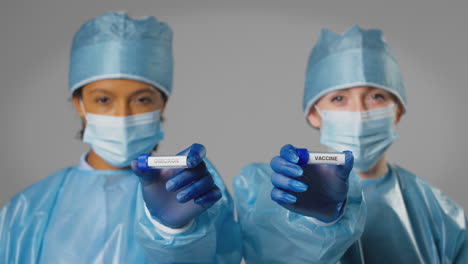 studio shot of female lab research workers in ppe holding test tubes labelled omicron and vaccine