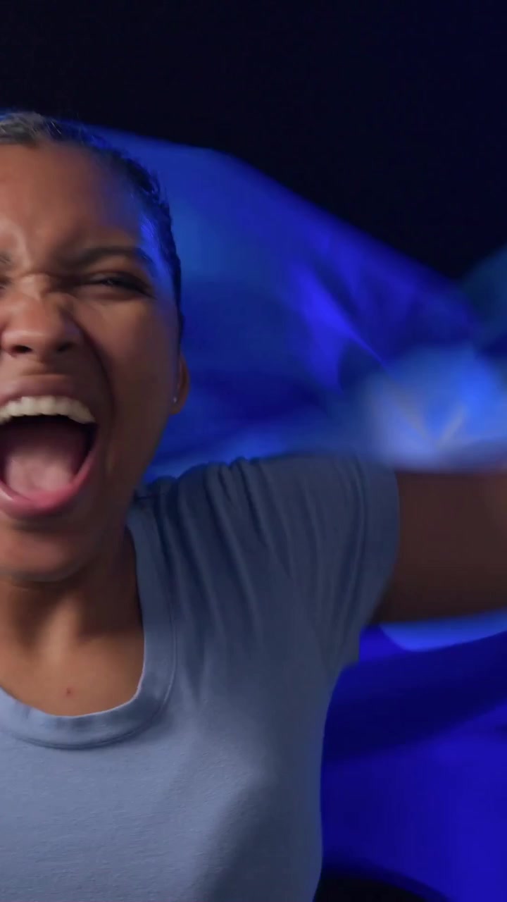 Vertical video: Waving woman blue tee raising blue flag from left in studio, cheering, copy space