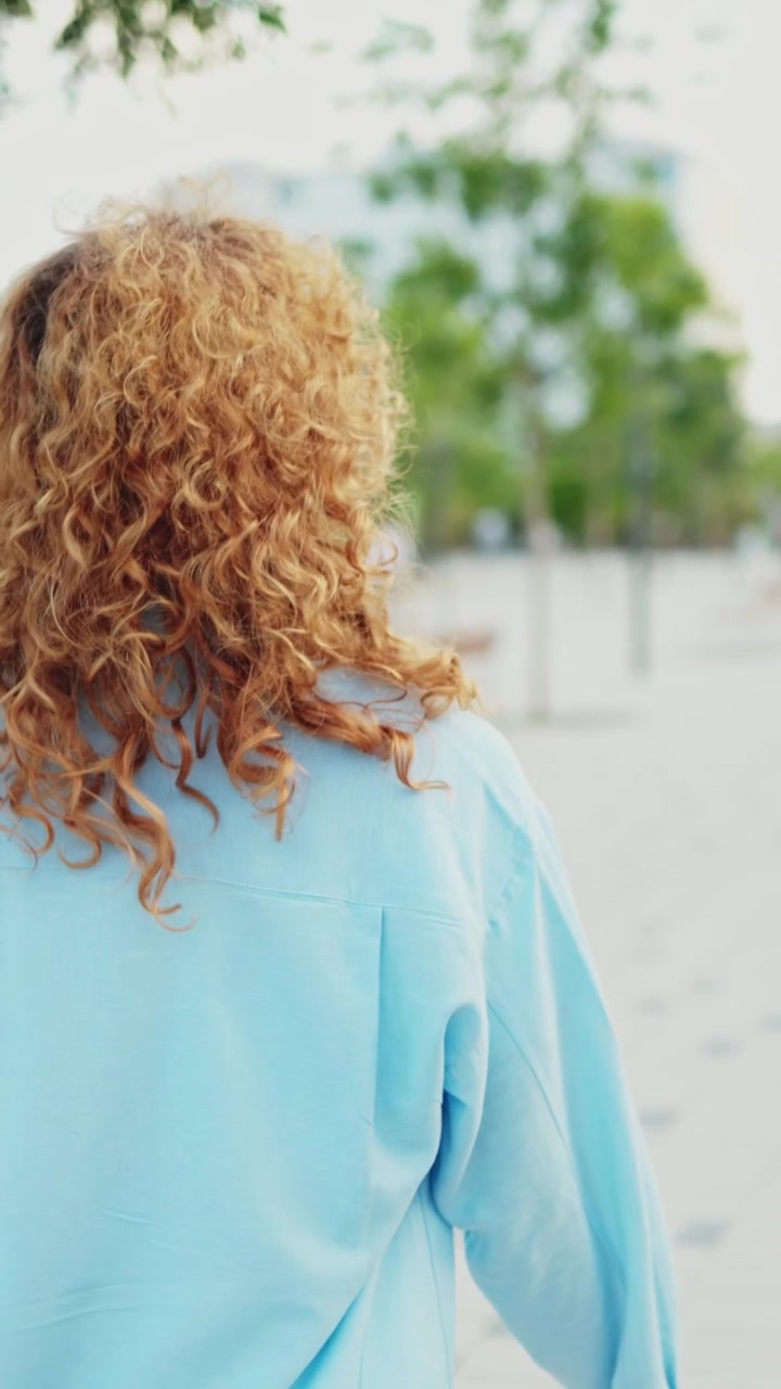 Vista trasera de una mujer con cabello rojo rizado caminando en un parque