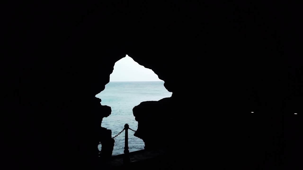 穏やかな海と水平線が背景に見える、自然の岩窟の開口部を通した海の眺め。暗いシルエットのフレームを形成。