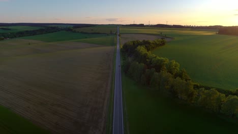 aerial drone birds eye view of european countryside road at sunset with wind turbines on the horizon in czech republic