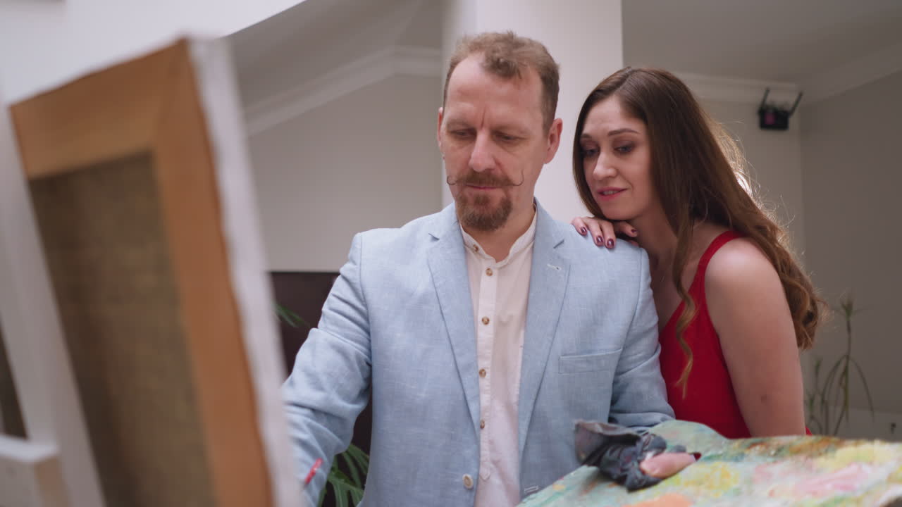 художественное сотрудничество между мужчиной и женщиной. женщина-муза в элегантном красном платье служит вдохновением, вдыхая жизнь в творчестве художника. создавая шедевр