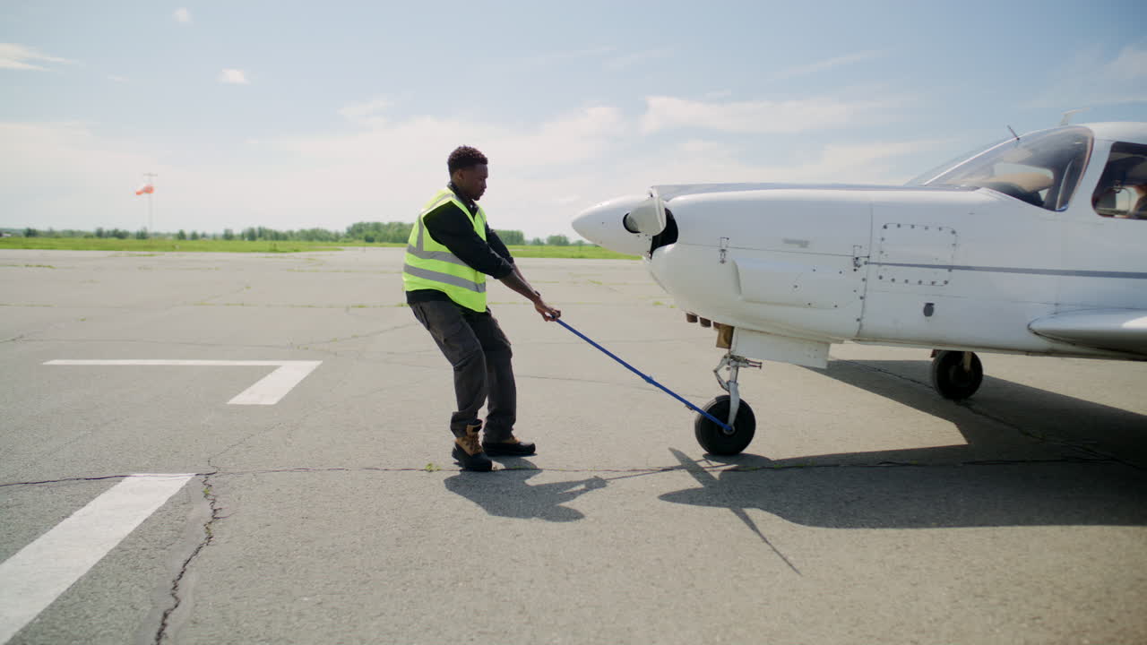Black Technician Pulling Small Aircraft across Sunny Airfield