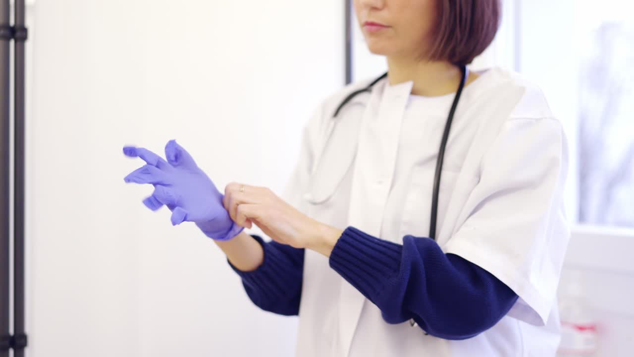 Unrecognizable female doctor putting on latex gloves in a clinic