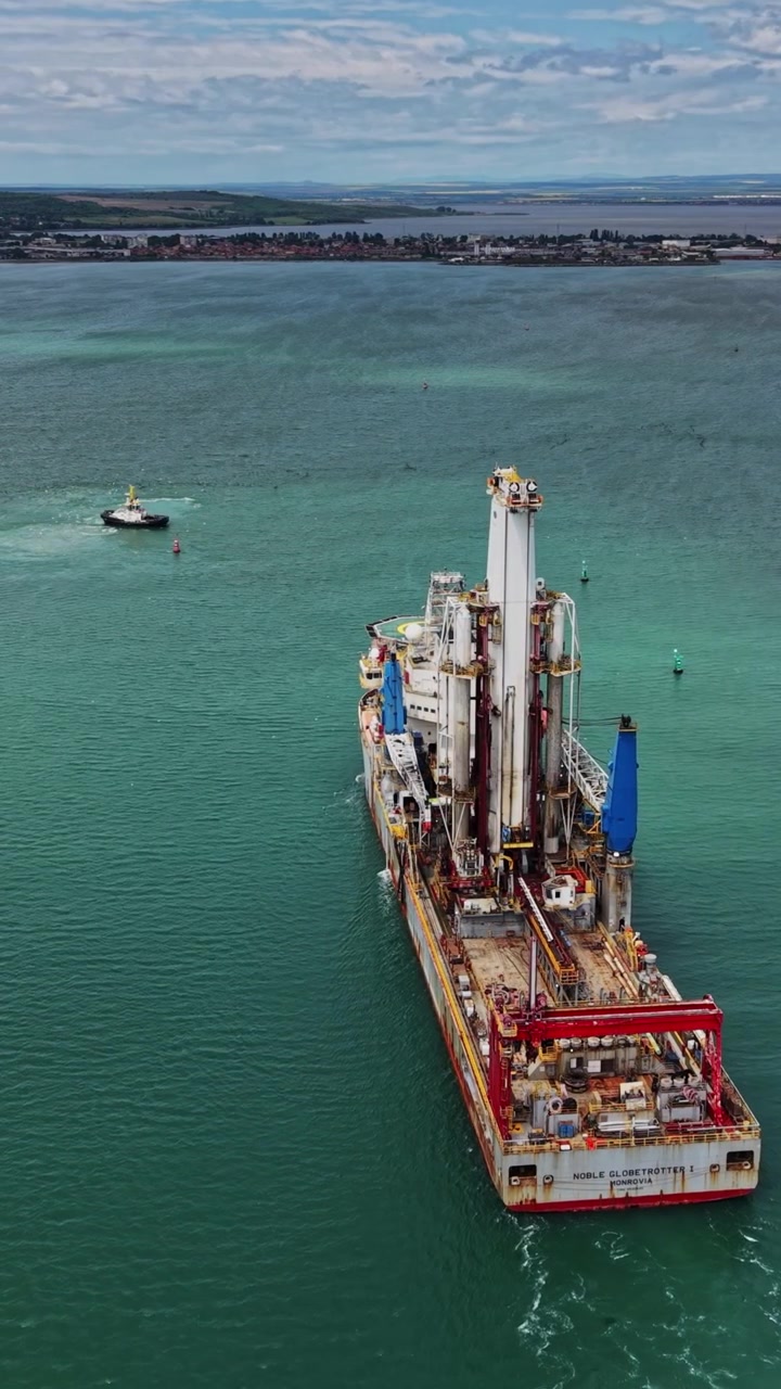 Tugboat guides large drilling vessel in coastal water near port