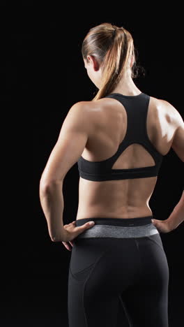 vertical video: caucasian female athlete showing strong back muscles, black background