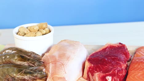 una vibrante exhibición de varios alimentos proteicos, incluidas carnes, mariscos y nueces contra un fondo azul
