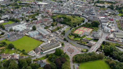 High-angle-view-of-tennis-courts-and-large-roundabout-on-river-waterfront.-Tilt-up-reveal-of-panoramic-view-of-town.-Ennis,-Ireland