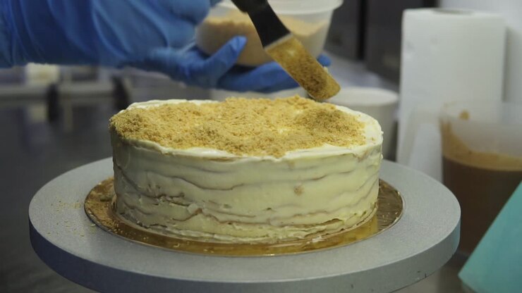 Covering Napoleon cake with grinded bread and spreading it evenly on top with confectioner spatula. Sprinkling cake with scrumbs. Traditional recipe of delicious cake.