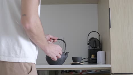 man pouring tea from teapot onto the cup