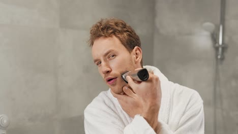 curly handsome guy shaves his beard with a clipper