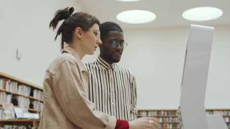 hombre y mujer multiétnicos usando una exhibición interactiva en la biblioteca