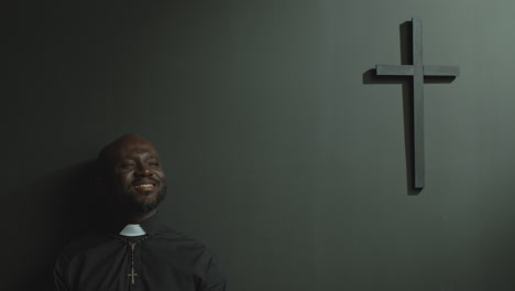 happy priest in cassock standing in modern church and smiling