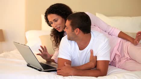 una pareja joven acostada en su cama usando una computadora portátil