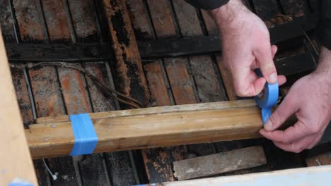 Closeup of hands wrapping thin blue tape around wooden beam seat in traditional irish boat