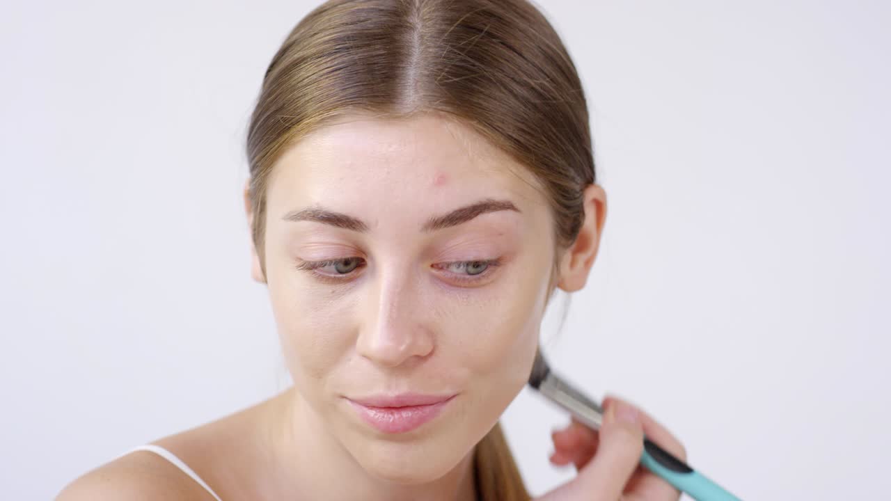 mujer atractiva poniendo en la fundación con el pincel