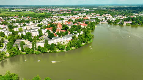 Vista-Aérea-De-Iława,-Que-Destaca-La-Pintoresca-Orilla-Del-Lago,-La-Exuberante-Vegetación-Y-Las-Zonas-Residenciales-De-La-Ciudad-Con-Edificios-Históricos,-Lo-Que-Proporciona-Un-Pintoresco-Paisaje-De-Verano.