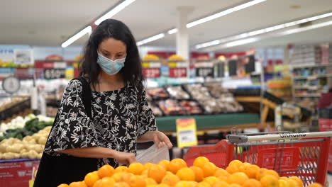 Una-Joven-Latina-Con-Una-Máscara-Facial-Revisa-Las-Naranjas-En-Busca-De-Frescura-En-Una-Tienda-De-Comestibles