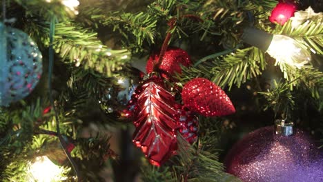 arranging shiny red ornaments on decorated christmas tree with lights