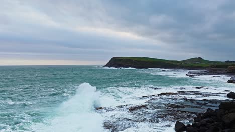 Aerial-dolly-soars-past-cliff-edge-as-waves-erupt-crashing-on-rocks