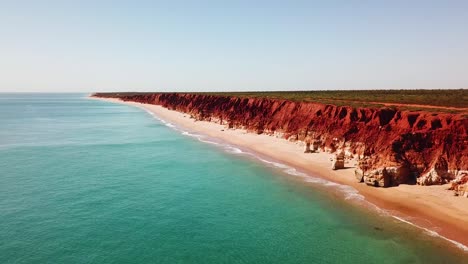 drone flying adjacent to spectacular red ocean side cliffs and blue water of western australia