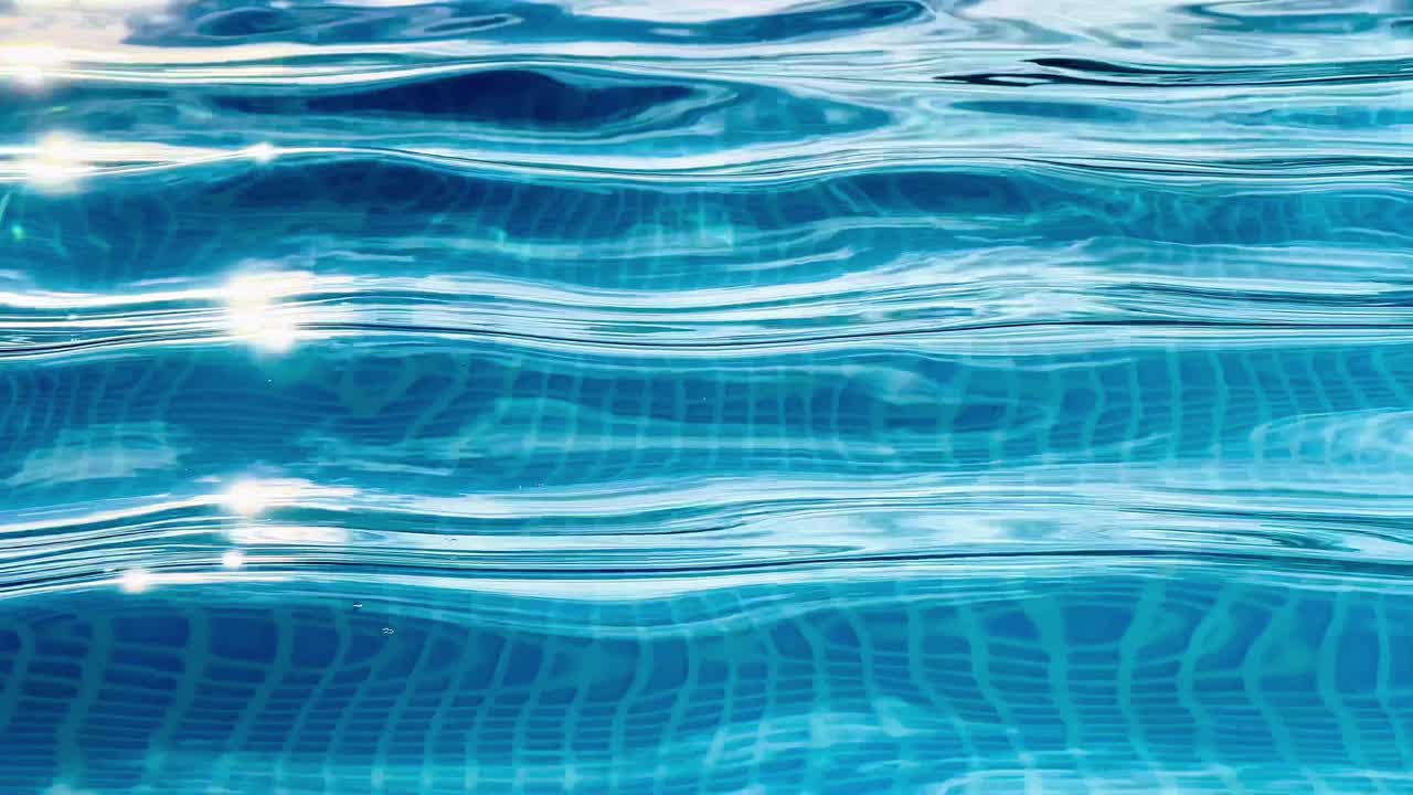 Air sebening kristal beriak lembut di kolam renang, permukaannya memantulkan sinar matahari dan menyingkap ubin mosaik biru di bawahnya, menciptakan pemandangan musim panas yang memukau dan menyegarkan.