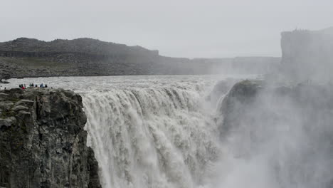 tourists look on at the immense power of the dettifoss waterfall in iceland