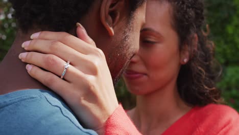 primer plano de una feliz mujer biracial con anillo de compromiso en la mano abrazando a su prometido