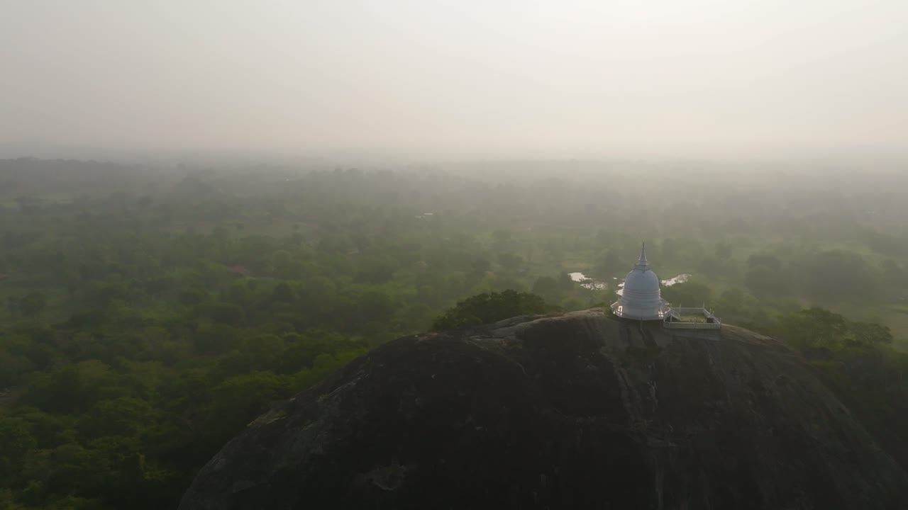 A serene white temple stands above the green canopy with misty plains beyond in Sri Lanka
