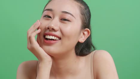 스튜디오에서 녹색 스크린 배경에 서있는 동안 그녀의 얼굴을 들고 카메라에 미소 짓는 아시아 여성의 근접