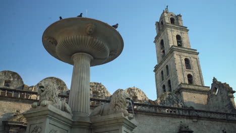 a view of the historic town square in la habana, cuba, where birds soar freely overhead and a child delights in playing by the fountain