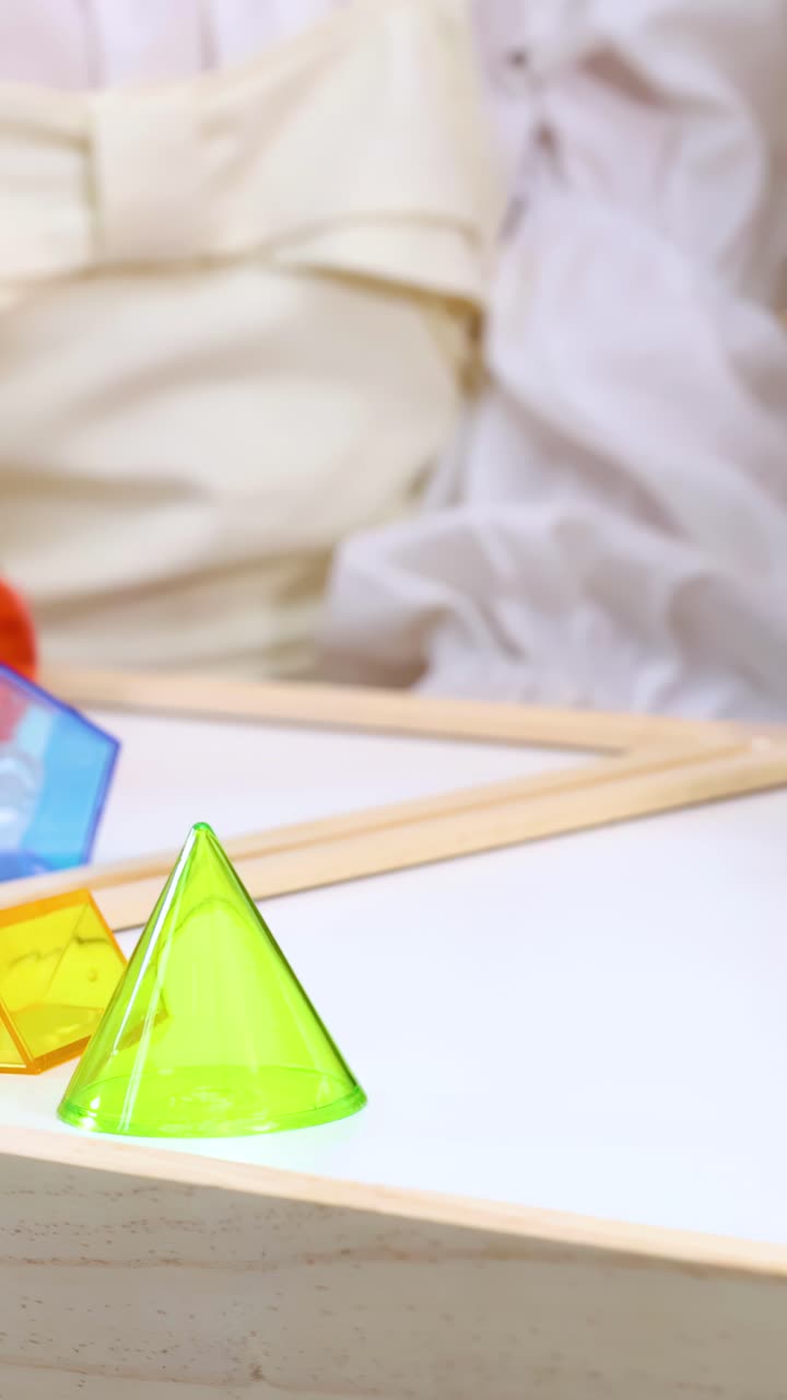 Mãos de criança exploram blocos geométricos coloridos em uma mesa de sala de aula com iluminação suave e brilhante