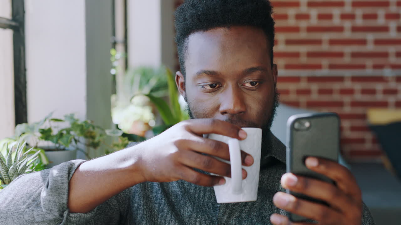 hombre negro, teléfono y beber café por apartamento