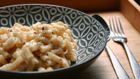 pan across macaroni cheese meal on wooden tray with cutlery