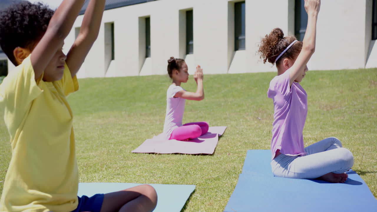 Biracial children practice yoga outdoors on colorful mats in school