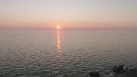 Beautiful-aerial-view-of-vibrant-high-contrast-sunset-over-calm-Baltic-sea,-clouds-at-the-horizon,-Karosta-war-port-concrete-coast-fortification-ruins-at-Liepaja,-wide-drone-shot-moving-forward