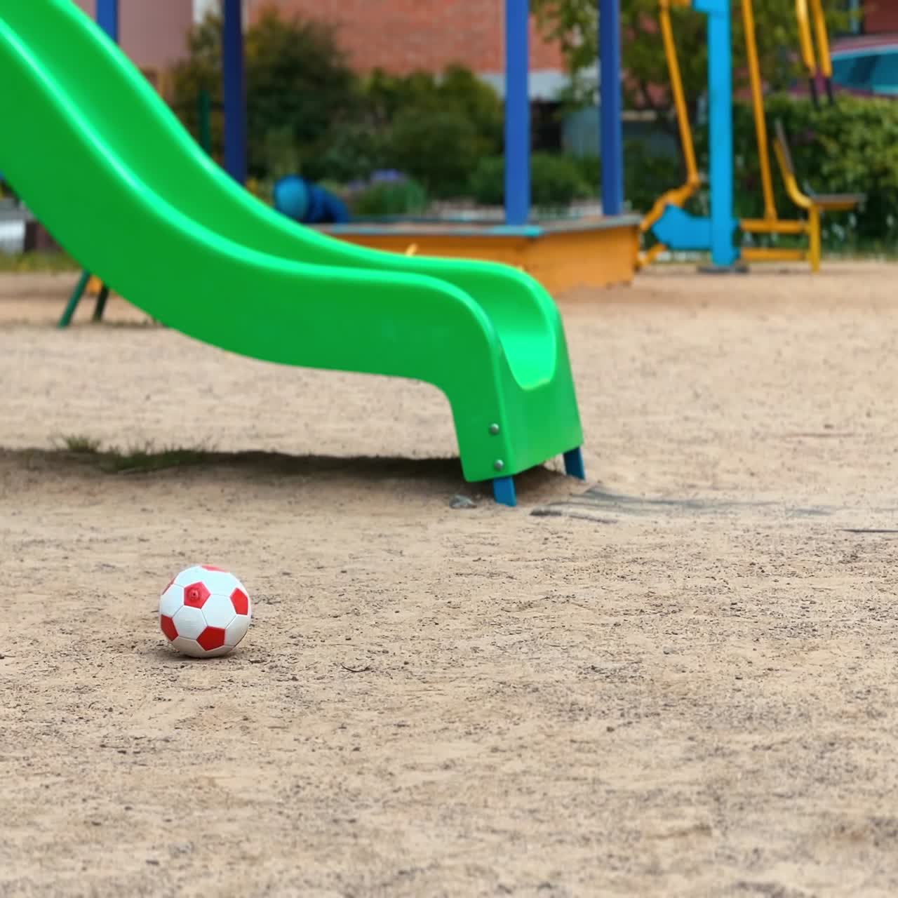 Active toddler runs by the playground and takes a ball from ground. Smiling kid approaches camera