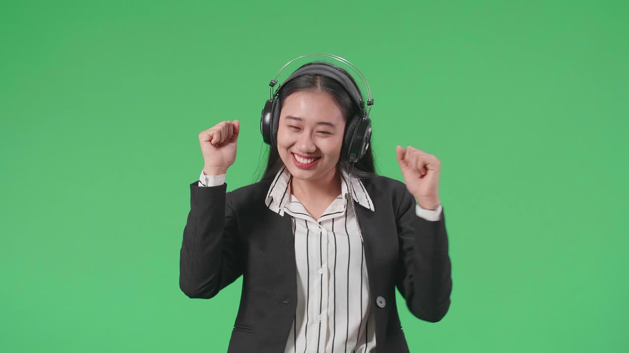An Asian Business Woman Listening To Music With Headphones And Dancing In The Green Screen Studio