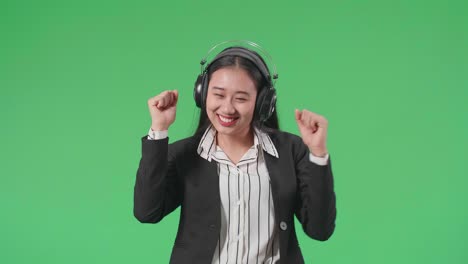 an asian business woman listening to music with headphones and dancing in the green screen studio