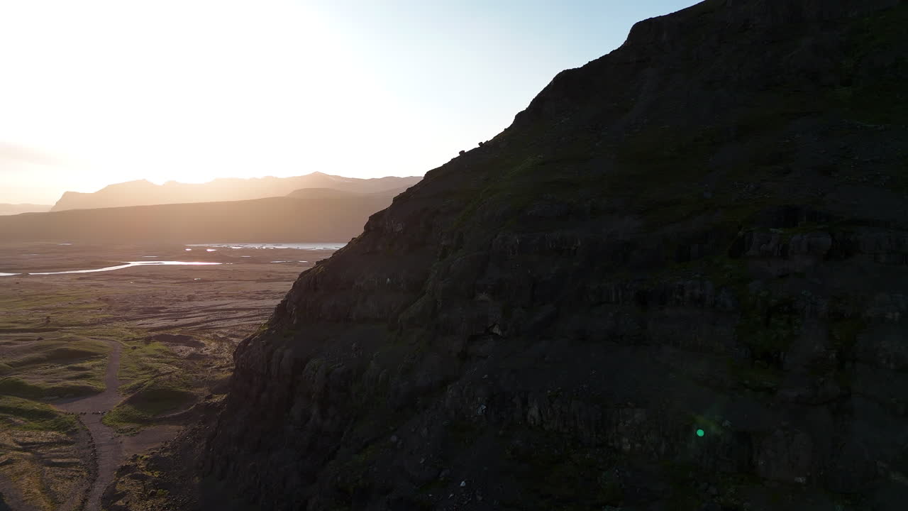 Vista aerea del ghiacciaio Svínafellsjökull al tramonto, che mostra profondi crepacci nel ghiaccio che confluiscono in una laguna glaciale scura, incorniciata da ripide montagne vulcaniche e dalla calda luce serale nell'Islanda meridionale