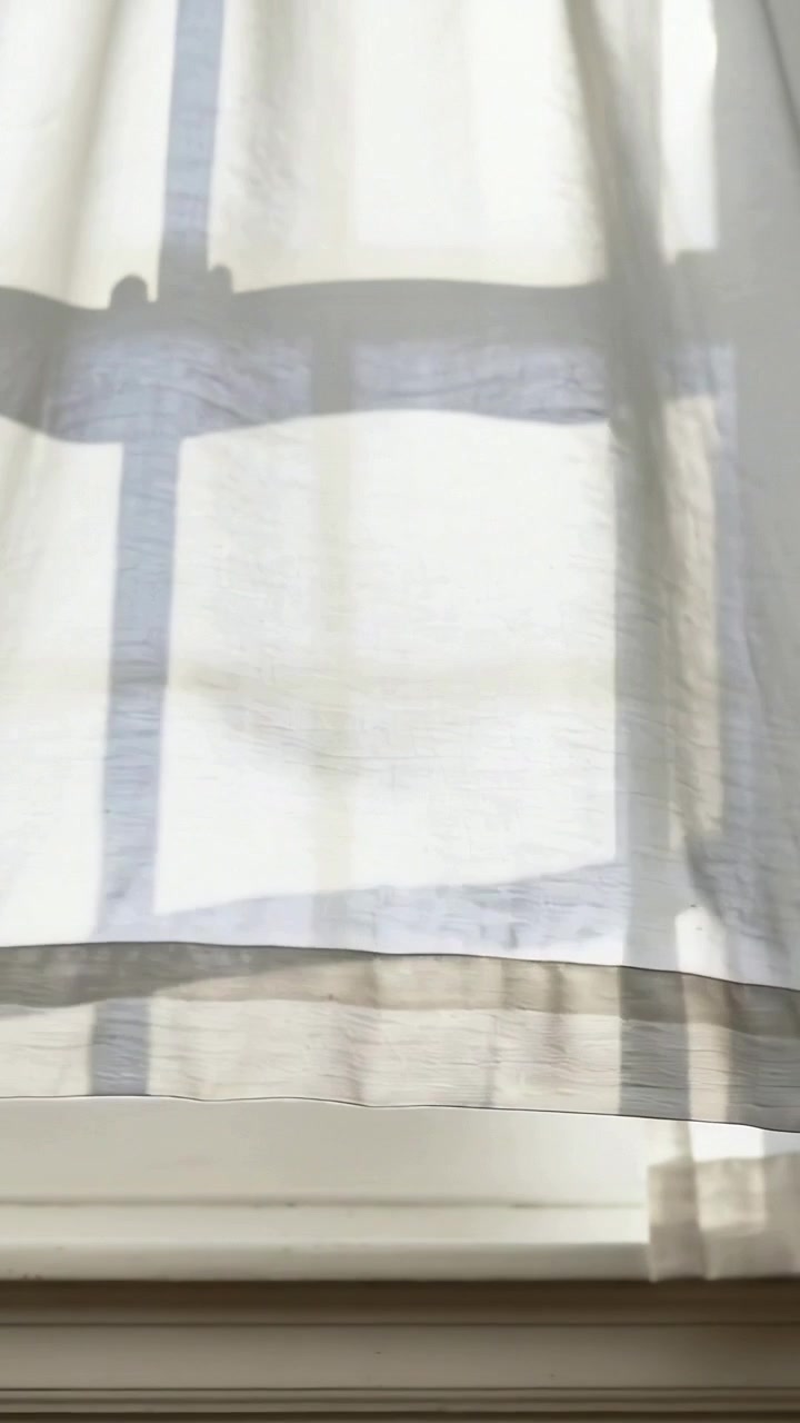 Vertical video: Billowing sheer check curtain over windowsill, breeze moving muntin shadows