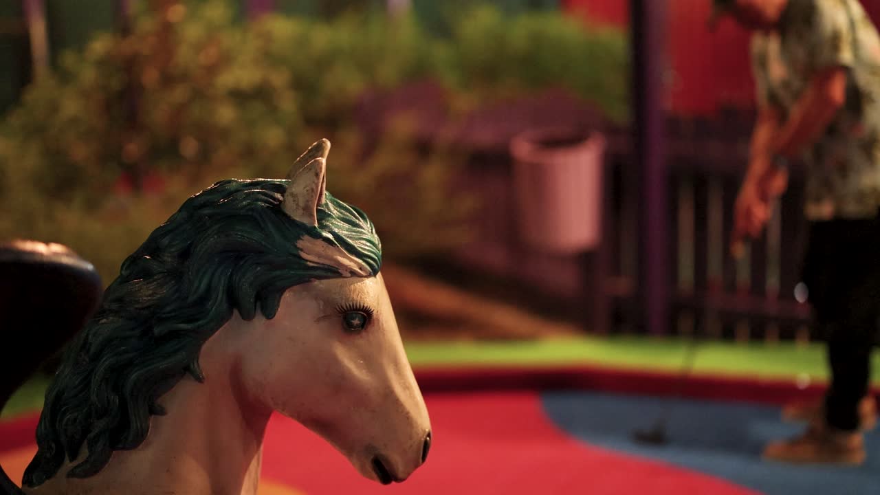 A man plays mini-golf at night near a horse statue. Vibrant colors and playful atmosphere enhance the scene