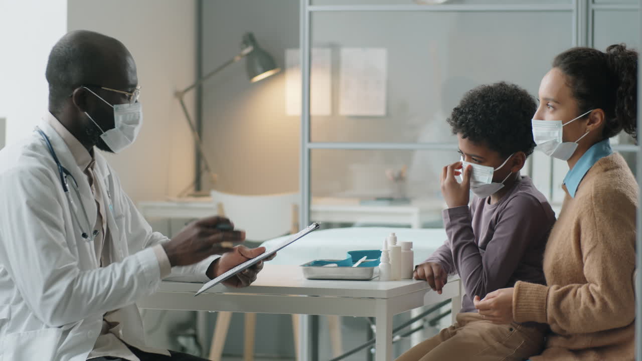 African American Boy and His Mother in Masks Having Consultation with Pediatrician