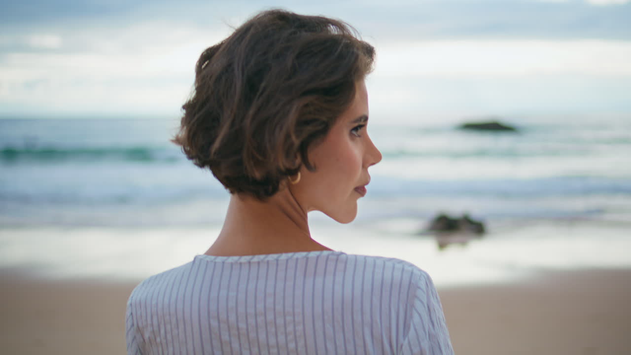 Primo piano di donna che passeggia in spiaggia in una giornata estiva nuvolosa. Donna sorridente che si gira verso l'oceano.