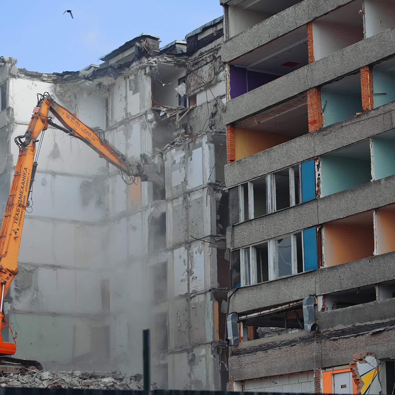 Compact orange demolishing machine dismantling the house. Deconstruction of a building ruined by the nature disaster. View from below