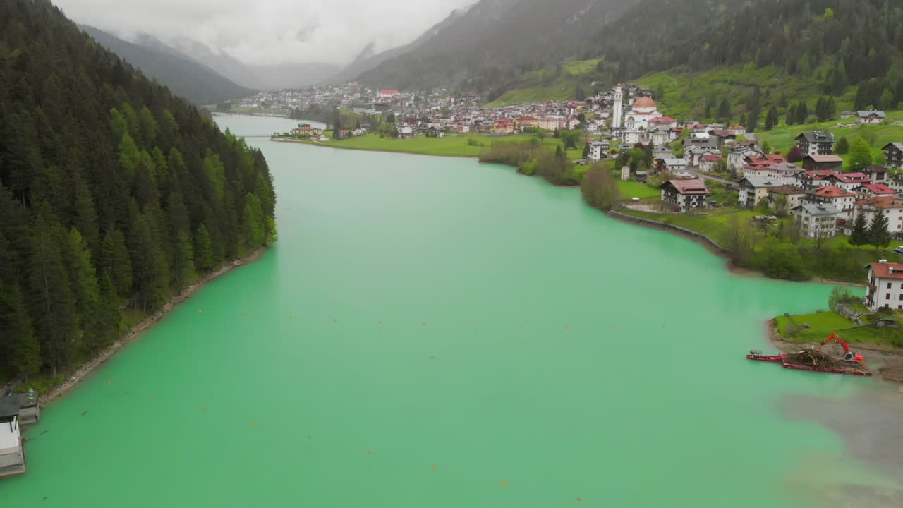 Un lago verde dietro una diga nelle Alpi italiane, diretto verso una città.