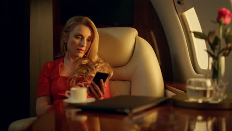 mujer rubia enviando mensajes por teléfono móvil en un avión privado en la luz dorada del sol.