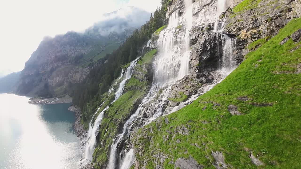 vuelo aéreo junto a una hermosa gran cascada en un paisaje montañoso, avión no tripulado volando sobre un lago azul - lago oeschinen, suiza